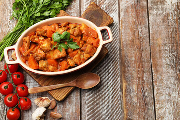 Delicious cooked stew in baking dish, fresh ingredients and spoon on wooden table, flat lay. Space for text