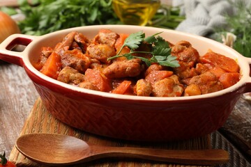 Delicious cooked stew in baking dish and spoon on wooden table, closeup