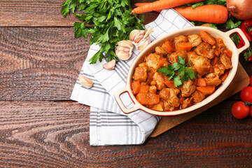 Delicious cooked stew in baking dish and fresh ingredients on wooden table, flat lay. Space for text