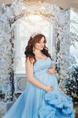 pregnant girl in a lush blue dress. girl with dark hair wearing a crown. christmas decoration. High quality photo