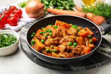 Delicious cooked stew in frying pan and ingredients on grey table, closeup