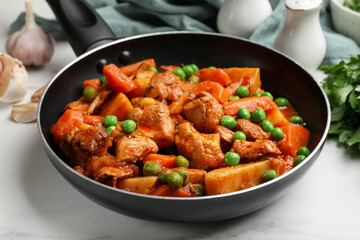 Delicious cooked stew in frying pan on white marble table, closeup