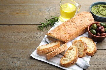 Cut ciabatta, spices and olives on wooden table, closeup. Space for text