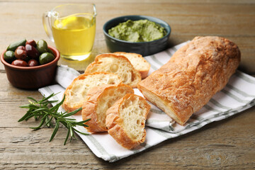 Cut ciabatta, spices and olives on wooden table, closeup