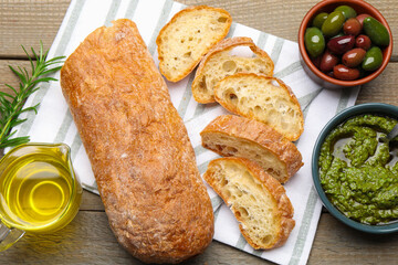 Cut ciabatta, spices and olives on wooden table, flat lay