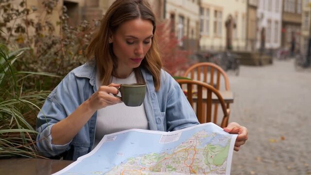 A woman engrossed in a map, sipping a beverage at a cafe, planning her next adventure. The image evokes a sense of travel, exploration and discovery. Stock Video