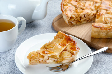Piece of delicious homemade apple pie, fork and tea on grey textured table, closeup