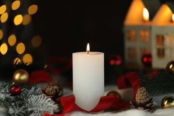 Burning candle, cones, fir tree branches and baubles on light blanket against black background with blurred lights, closeup. Bokeh effect