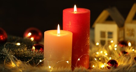 Burning candles, fir tree branches, baubles and festive lights on faux fur against black background, closeup. Christmas greeting card