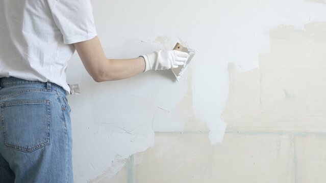 Unknown female construction worker applying plaster with putty knife, smoothing wall surface during home renovation, fixing wall imperfections with professional drywall repair technique, close up