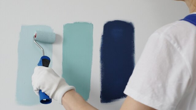 Painter wearing protective gloves rolling blue paint on white wall, creating gradient color effect for home interior renovation project