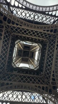 Extreme low-angle vertical shot capturing the dizzying, symmetrical, and abstract geometric patterns of the iconic Eiffel Tower's iron framework.