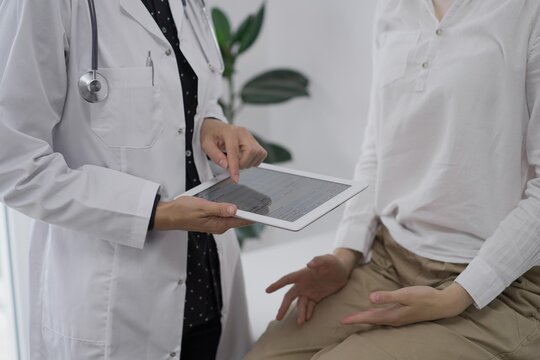 Doctor and a patient. The female physician is using a tablet computer besides a young woman during a consultation in the clinic, view above. Medicine concept - Powered by Adobe