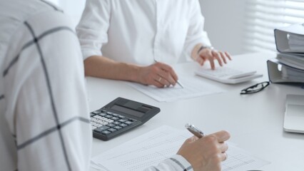 Unrecognizable accountants working together in a well lit office, analyzing financial data and preparing reports with calculators and pens. Audit and taxes in business