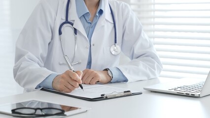 Healthcare professional documenting patient information while working with digital devices in a minimalist white workspace. Medicine and health care concept