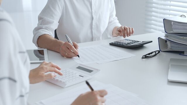Professional accountants collaborating in a well lit office, analyzing financial data and preparing reports with calculators and pens. Audit and taxes
