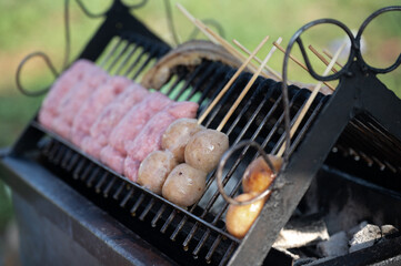 Grilled sausage skewer street food thailand aroma rising from charcoal grill with rustic metal rack outdoors, warm afternoon light adds cozy mood and local flavor to tasty snack scene
