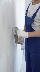 Professional construction worker wearing blue work overall is using a finishing trowel to carefully apply plaster on a wall, demonstrating expertise in home renovation