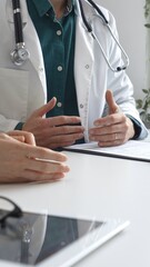 Doctor man wearing medical coat over green shirt, and stethoscope is gesturing with hands while explaining diagnosis to patient during medical consultation in clinic office. Medicine and health care