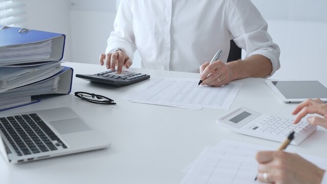 Two accountants collaborating in a well lit office, analyzing financial data and preparing reports with calculators and pens. Audit and taxes in business