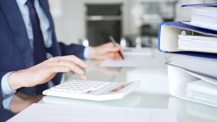 Accountant working in office, calculating finance data using black calculator and taking notes for budget planning. Audit and taxes in business - Powered by Adobe