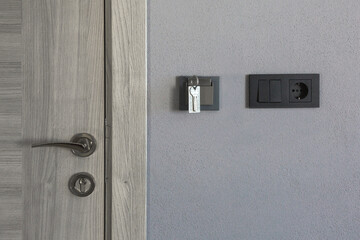 Modern hotel room interior with a wooden door, metal handle, and key inserted into an energy-saving switch on a gray wall, symbolizing security, comfort, and smart accommodation design
