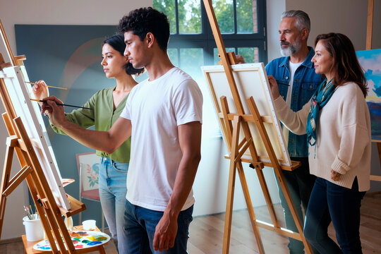 Multiethnic group of young adult and middle aged men and women painting on canvases in art studio, focusing on creative process, standing side by side and using brushes