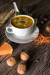 vegetable cream soup  with cream swirls and pumpkin seeds, served on rustic wood with walnuts and shredded carrots