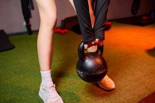 Braided aired woman performing weightlifting in dimly lit studio, Dedicated woman with braided hair executing strenuous kettlebell exercise in moody training environment