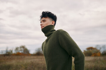 Young man in a green turtleneck sweater stands in a windswept field, captured with authenticity and...