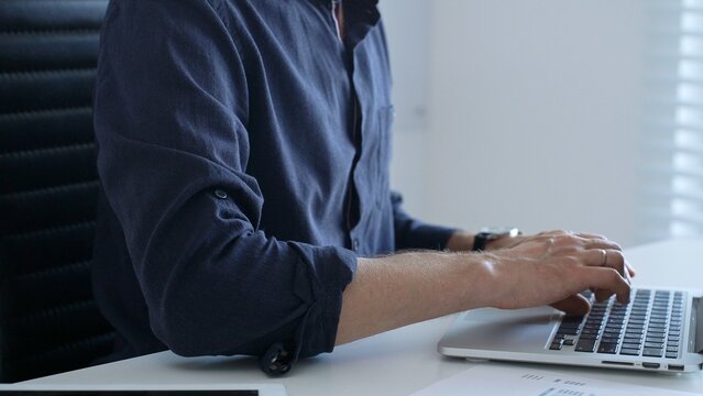 Professional businessman typing on laptop, surrounded by financial reports and digital tablet, working in contemporary corporate workspace. Business people concept