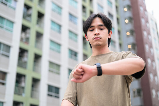 Portrait of handsome Young Asian Thai man using smartwatch outdoors low angle view - Powered by Adobe