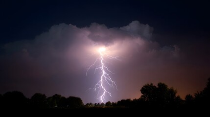 A bright lightning bolt strikes through a dark stormy night sky illuminating dramatic clouds above silhouetted trees