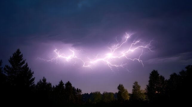 Dramatic lightning illuminates a dark stormy night sky above a silhouetted forest