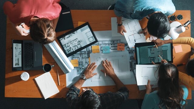 Top down view of manager writing project plan and sitting at meeting. Aerial view of business people planning and sharing idea about house construction at table with laptop and equipments. Symposium. - Powered by Adobe