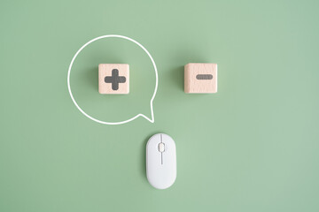 For positive and negative, thinking   opposites, pros and cons concept, top view of wooden cube block with plus, inside speech bubble, and minus sign, wireless mouse on green background