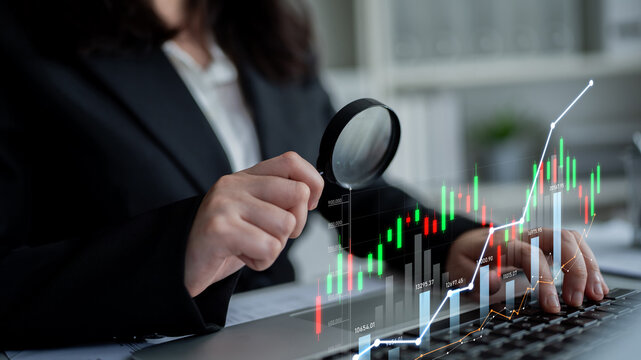 Professional examines financial data trends using a magnifying glass, emphasizing stock market charts in a modern office environment focused on analysis and growth. Scalp