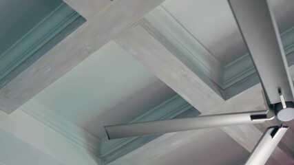 Wooden beams cross soft blue ceiling in clean lines. Light colors and smooth shapes make space feel fresh and open. Fan adds modern touch to calm design.