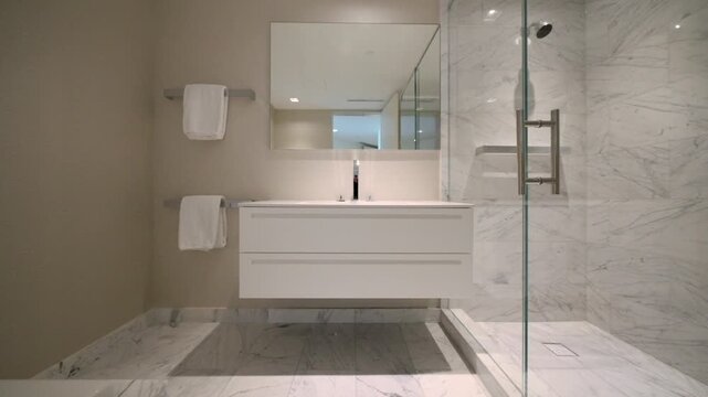 Marble walls and glass shower make bathroom feel calm and clean. White towels and soft light add gentle touch. Space feels fresh, modern and quietly elegant.
