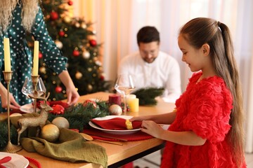Little girl setting table with her mom in room decorated for Christmas