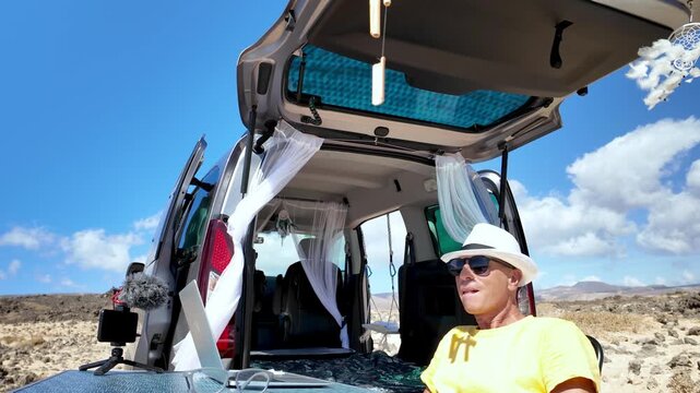 Mature male freelancer enjoying a break from his remote work, sitting by his customized minivan office in a scenic, arid landscape, embracing the digital nomad lifestyle and freedom
