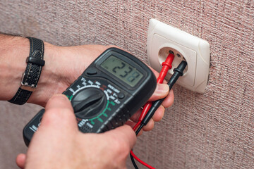 A man's hands measure the voltage in an electrical outlet using a multimeter