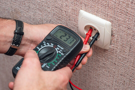 A man's hands measure the voltage in an electrical outlet using a multimeter