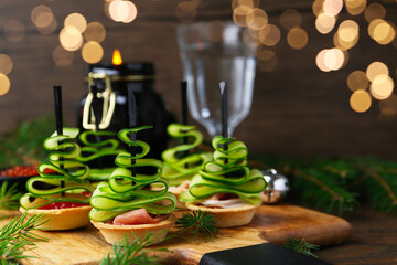 Christmas trees made with cucumber, red caviar, ham and festive decor on wooden table, closeup