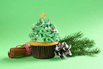 Christmas tree shaped cupcake, cinnamon and festive decor on green background, closeup
