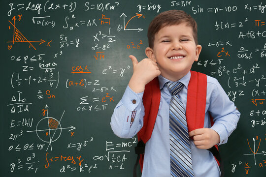 Cute little child showing thumbs-up near green chalkboard with formulas and drawings