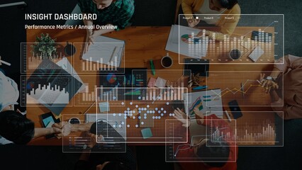 A diverse group of professionals collaborates in a modern workspace, analyzing performance metrics and data visualization charts during an annual overview meeting. Raster