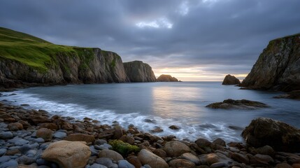 Obraz premium Rugged cliffs embrace a serene cove with waves lapping a pebble shore at twilight