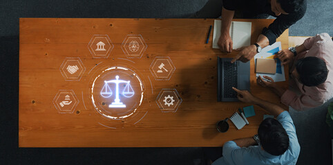 Aerial view of individuals collaborating over legal symbols and scales on a wooden desk,...