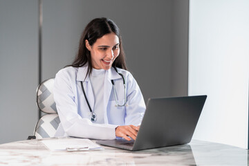 Female doctor working with a laptop in a modern medical office, focusing on healthcare consultation, digital technology, and professional service for patient care and online treatment.